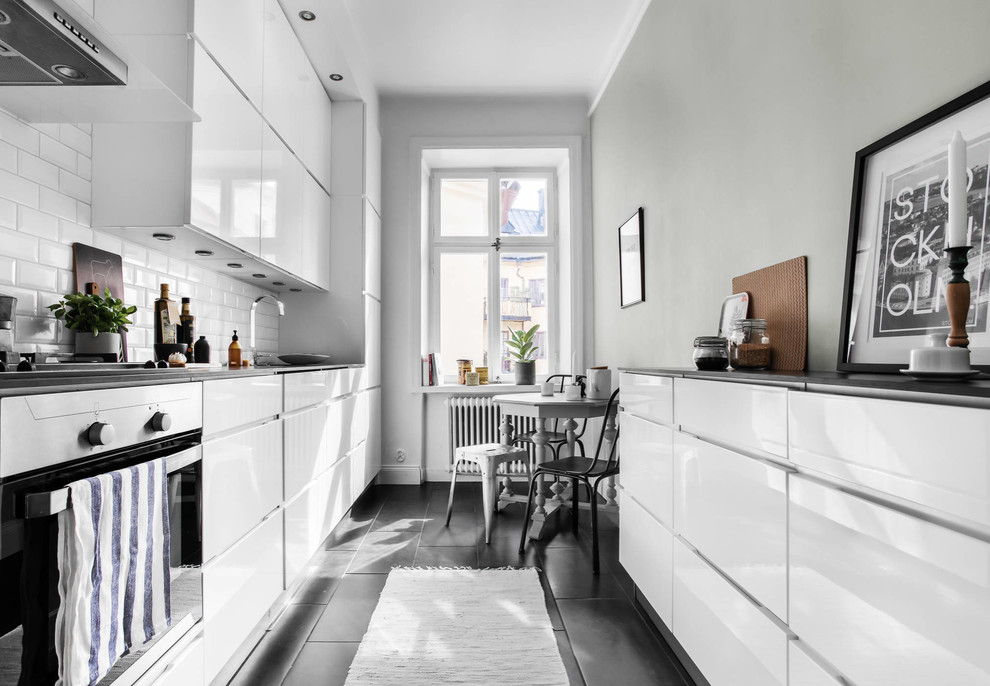 Idéer för ett minimalistiskt svart kök, med släta luckor, vita skåp, vitt stänkskydd, stänkskydd i tunnelbanekakel och svart golv