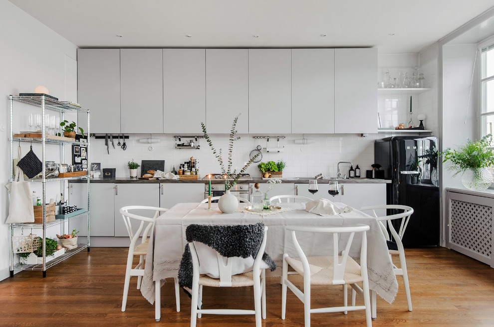 Eat-in kitchen - mid-sized scandinavian single-wall medium tone wood floor eat-in kitchen idea in Stockholm with flat-panel cabinets, gray cabinets, stainless steel countertops, white backsplash, black appliances and no island