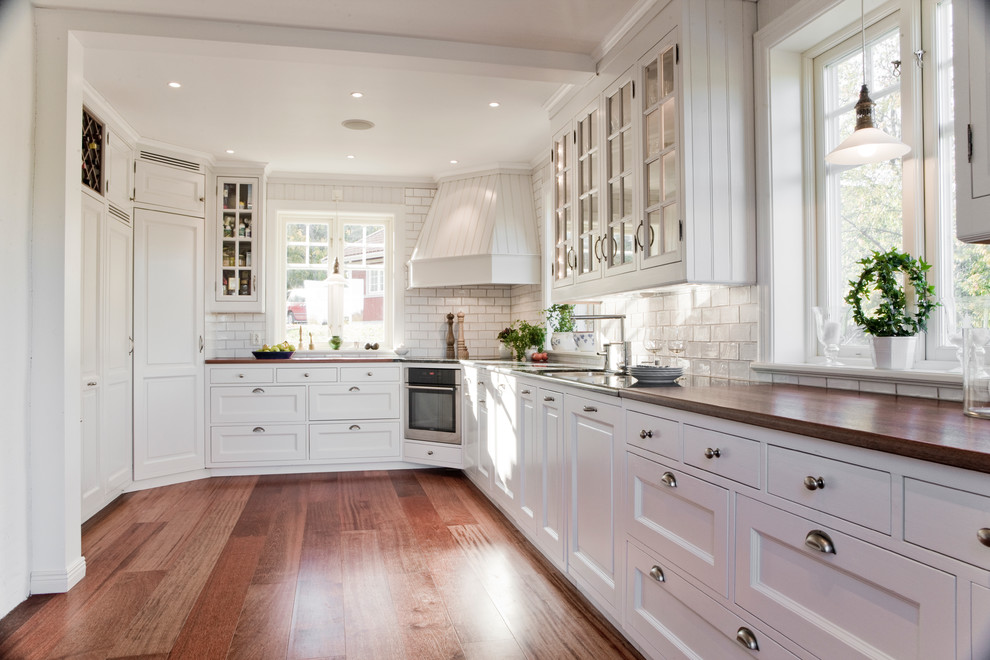 Foto på ett mellanstort lantligt kök, med en dubbel diskho, luckor med profilerade fronter, vita skåp, träbänkskiva, vitt stänkskydd, stänkskydd i keramik, integrerade vitvaror, mörkt trägolv och brunt golv