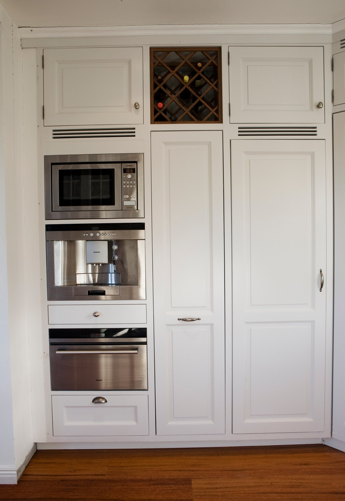 Bild på ett mellanstort vintage kök, med en dubbel diskho, luckor med profilerade fronter, vita skåp, träbänkskiva, vitt stänkskydd, stänkskydd i keramik, integrerade vitvaror, mörkt trägolv och brunt golv