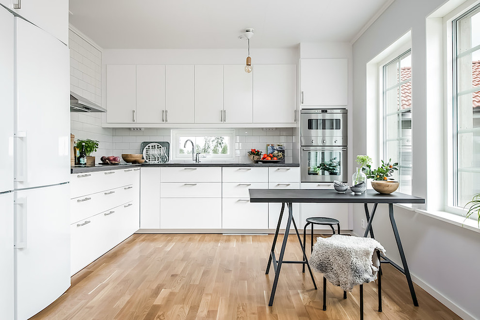 Inspiration for a scandi kitchen/diner in Other with flat-panel cabinets, white cabinets, white splashback, metro tiled splashback, stainless steel appliances, medium hardwood flooring, no island and brown floors.