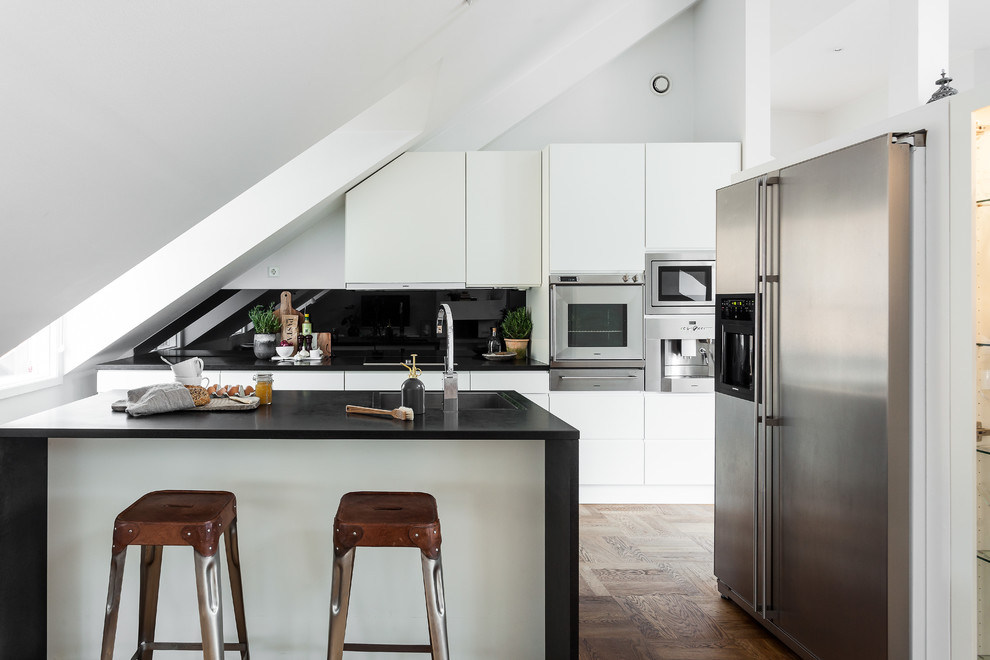 Inspiration for a mid-sized scandinavian galley light wood floor eat-in kitchen remodel in Stockholm with flat-panel cabinets, white cabinets, stainless steel appliances, an island, an integrated sink and black backsplash