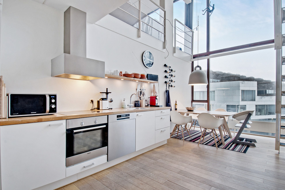 Foto på ett mellanstort nordiskt linjärt kök och matrum, med en nedsänkt diskho, släta luckor, vita skåp, träbänkskiva, rostfria vitvaror och ljust trägolv