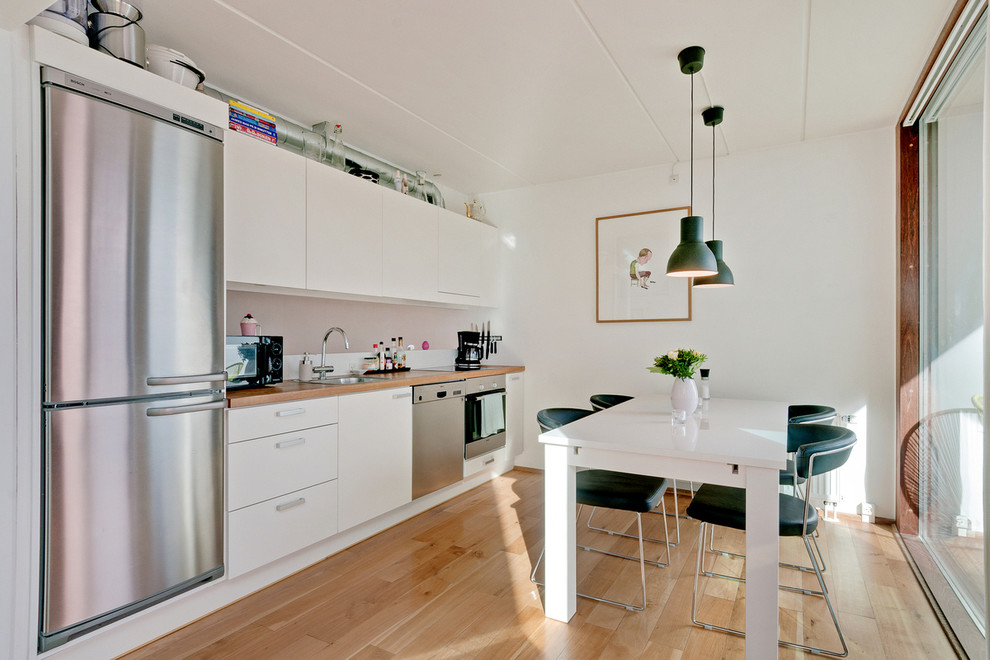Photo of a small scandi single-wall kitchen/diner in Copenhagen with a built-in sink, flat-panel cabinets, white cabinets, wood worktops, grey splashback, stainless steel appliances, light hardwood flooring and no island.