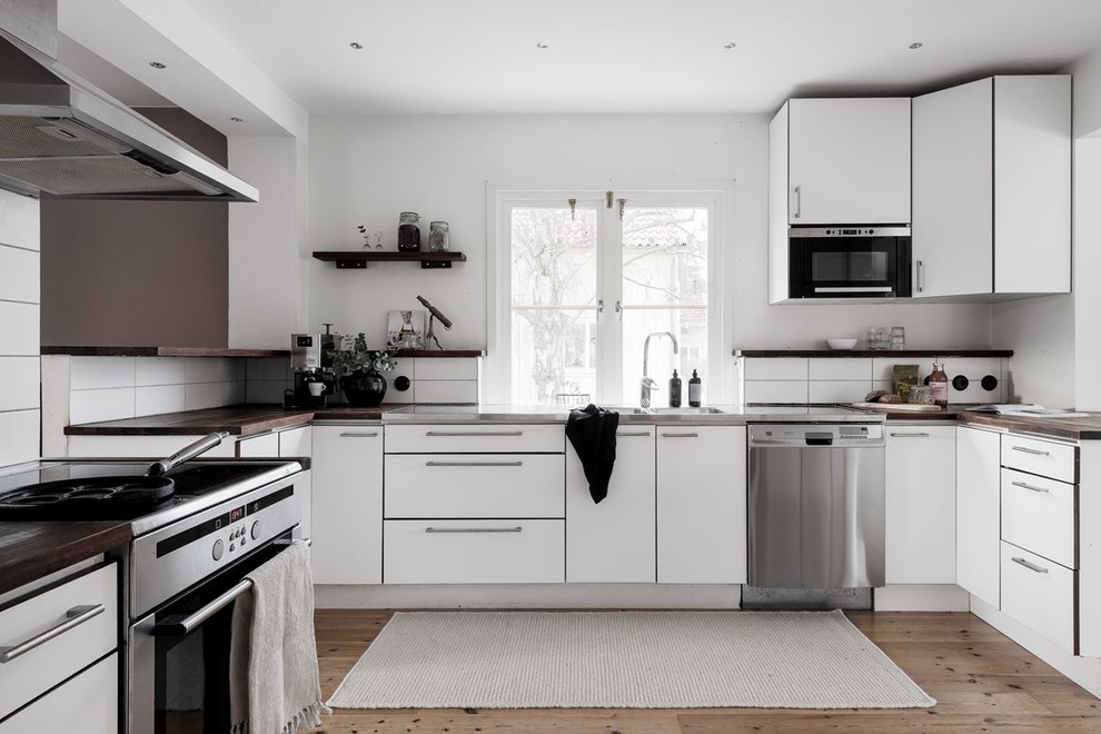 Inspiration for a mid-sized scandinavian u-shaped light wood floor and beige floor eat-in kitchen remodel in Stockholm with flat-panel cabinets, white cabinets, no island, a double-bowl sink, wood countertops, white backsplash, stainless steel appliances and brown countertops