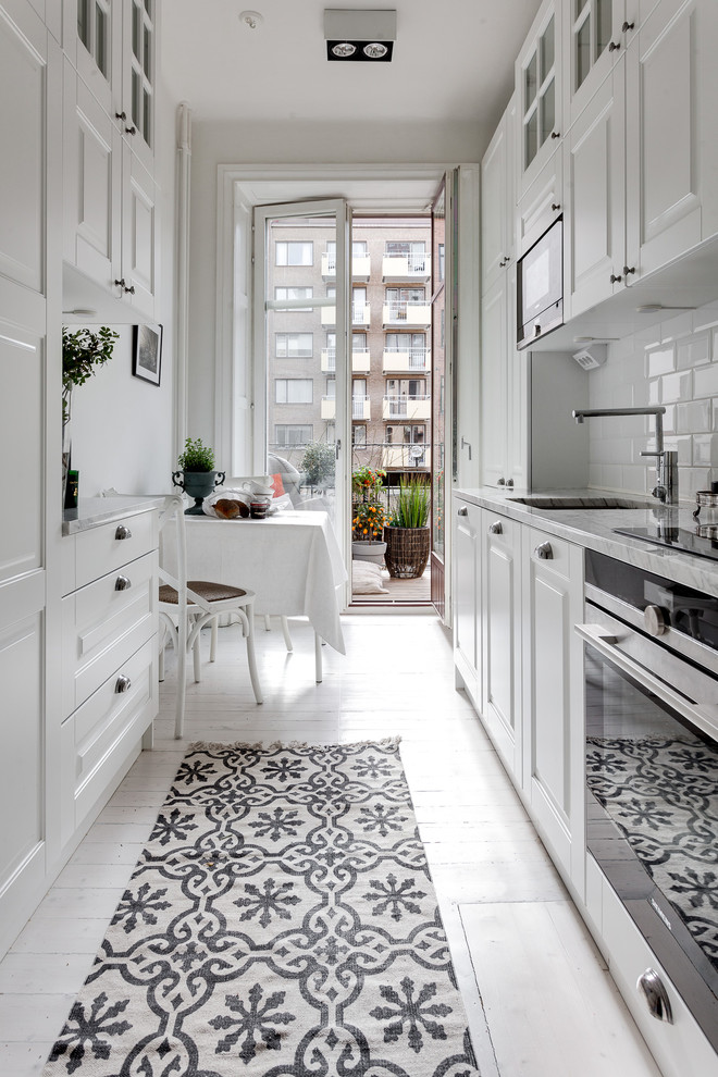 Eat-in kitchen - mid-sized scandinavian galley painted wood floor eat-in kitchen idea in Stockholm with an undermount sink, raised-panel cabinets, white backsplash, subway tile backsplash, stainless steel appliances and marble countertops