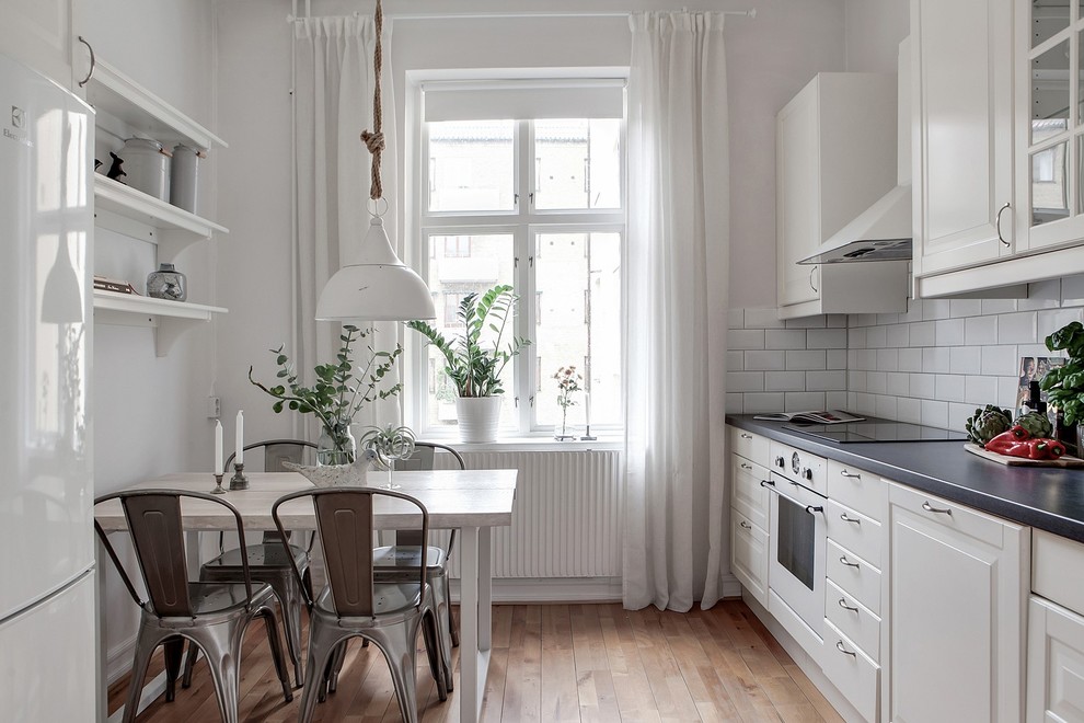 Idéer för att renovera ett minimalistiskt linjärt kök och matrum, med luckor med upphöjd panel, vita skåp, mellanmörkt trägolv, brunt golv, vitt stänkskydd, stänkskydd i tunnelbanekakel och vita vitvaror