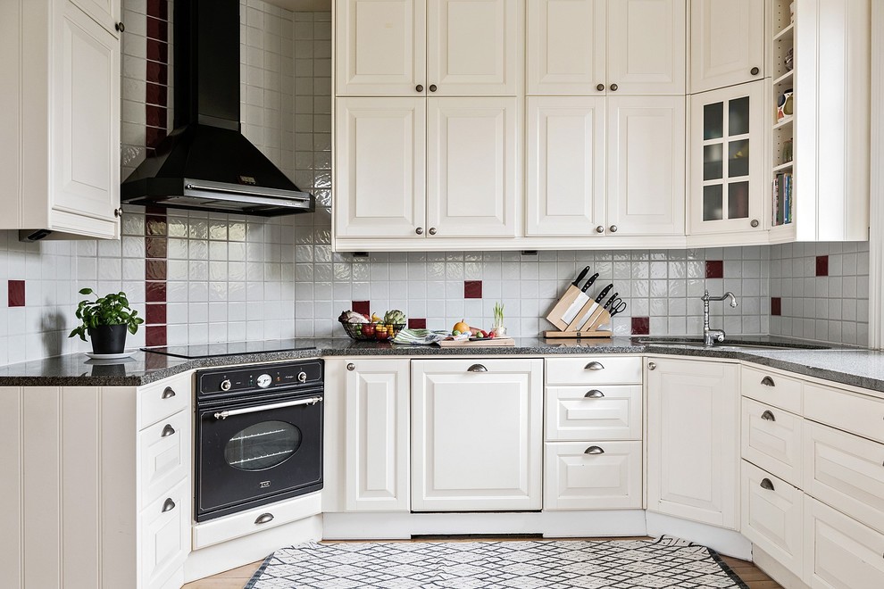 На фото: п-образная кухня среднего размера, со стиральной машиной в скандинавском стиле с белыми фасадами, гранитной столешницей, разноцветным фартуком, черной техникой и фасадами с выступающей филенкой без острова