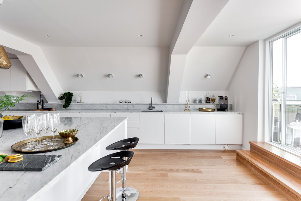 Foto på ett stort nordiskt linjärt kök och matrum, med en enkel diskho, släta luckor, vita skåp, marmorbänkskiva, mellanmörkt trägolv och en köksö