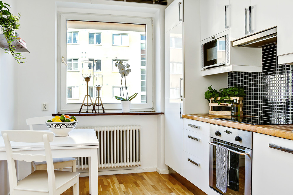 Exempel på ett mellanstort nordiskt linjärt kök, med släta luckor, vita skåp, träbänkskiva, svart stänkskydd, stänkskydd i mosaik, rostfria vitvaror och mellanmörkt trägolv