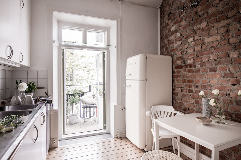 Bild på ett mellanstort minimalistiskt linjärt kök och matrum, med släta luckor, bänkskiva i rostfritt stål, vitt stänkskydd, ljust trägolv och beiget golv