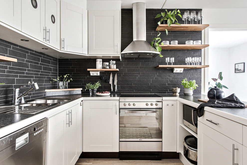 Idéer för minimalistiska svart u-kök, med en dubbel diskho, luckor med infälld panel, vita skåp, svart stänkskydd, rostfria vitvaror, ljust trägolv, en halv köksö och beiget golv