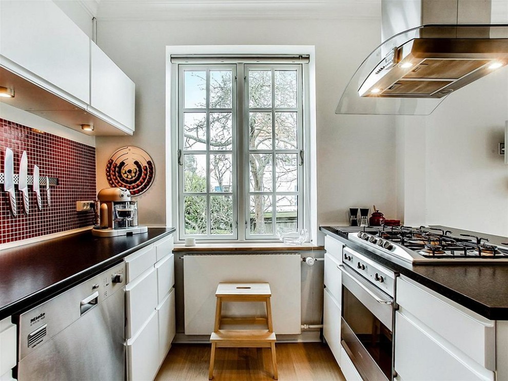 Medium sized scandinavian galley enclosed kitchen in Copenhagen with flat-panel cabinets, white cabinets, stainless steel appliances, medium hardwood flooring, no island and quartz worktops.