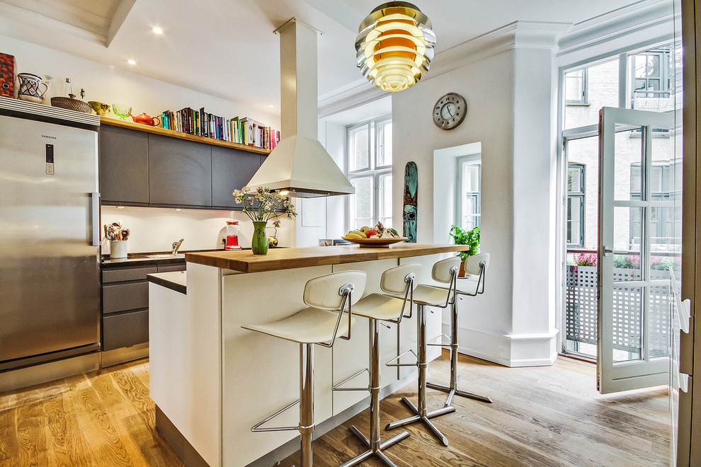 На фото: параллельная кухня-гостиная среднего размера в скандинавском стиле с плоскими фасадами, деревянной столешницей, техникой из нержавеющей стали, светлым паркетным полом, островом и черно-белыми фасадами с