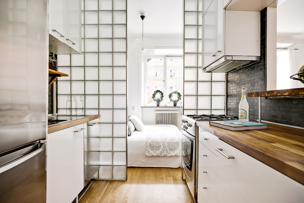 Свежая идея для дизайна: параллельная кухня в скандинавском стиле с плоскими фасадами, белыми фасадами, деревянной столешницей, серым фартуком, техникой из нержавеющей стали и паркетным полом среднего тона без острова - отличное фото интерьера