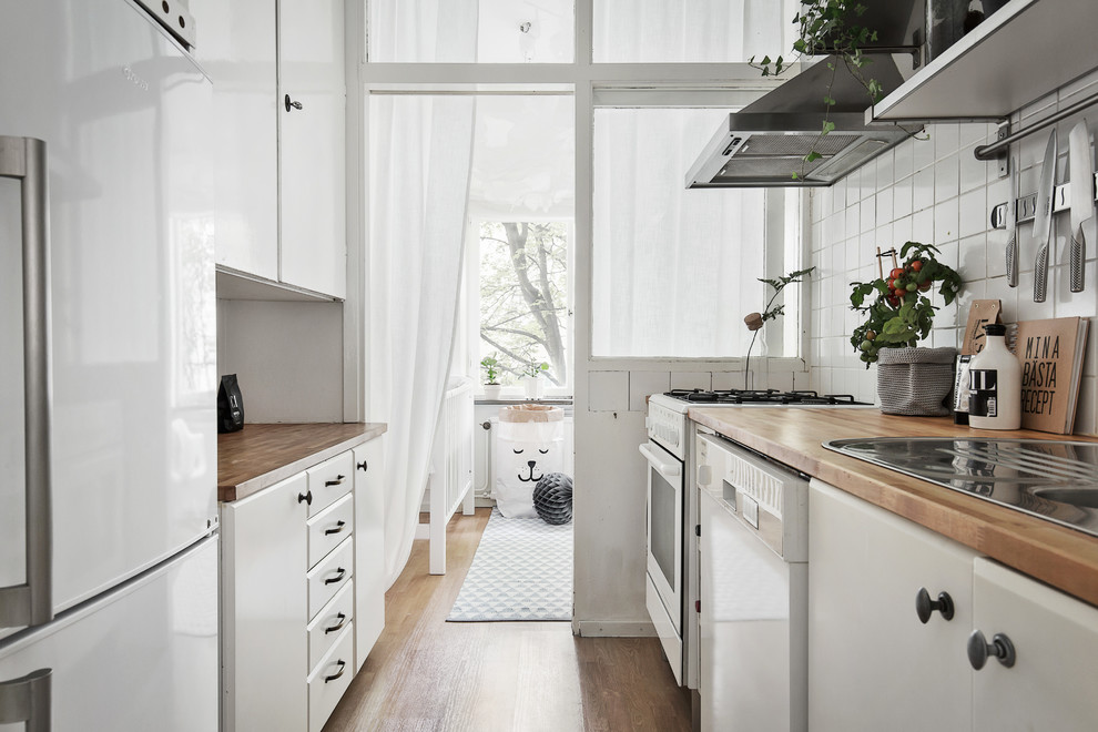 Design ideas for a scandinavian galley kitchen in Stockholm with a built-in sink, flat-panel cabinets, white cabinets, wood worktops, white splashback, stainless steel appliances, light hardwood flooring and no island.