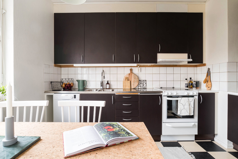 ストックホルムにある北欧スタイルのおしゃれなキッチン (ダブルシンク、フラットパネル扉のキャビネット、黒いキャビネット、ステンレスカウンター、白いキッチンパネル、磁器タイルのキッチンパネル、白い調理設備) の写真