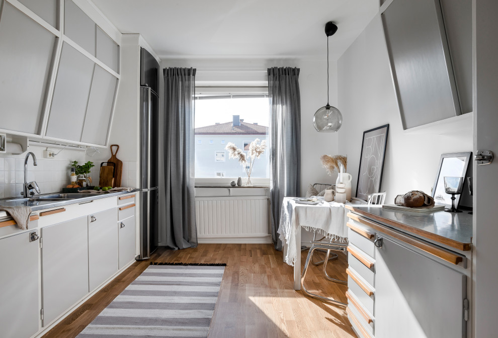 Zweizeilige, Kleine Skandinavische Küche mit Doppelwaschbecken, flächenbündigen Schrankfronten, grauen Schränken, Küchengeräten aus Edelstahl, braunem Boden und grauer Arbeitsplatte in Stockholm