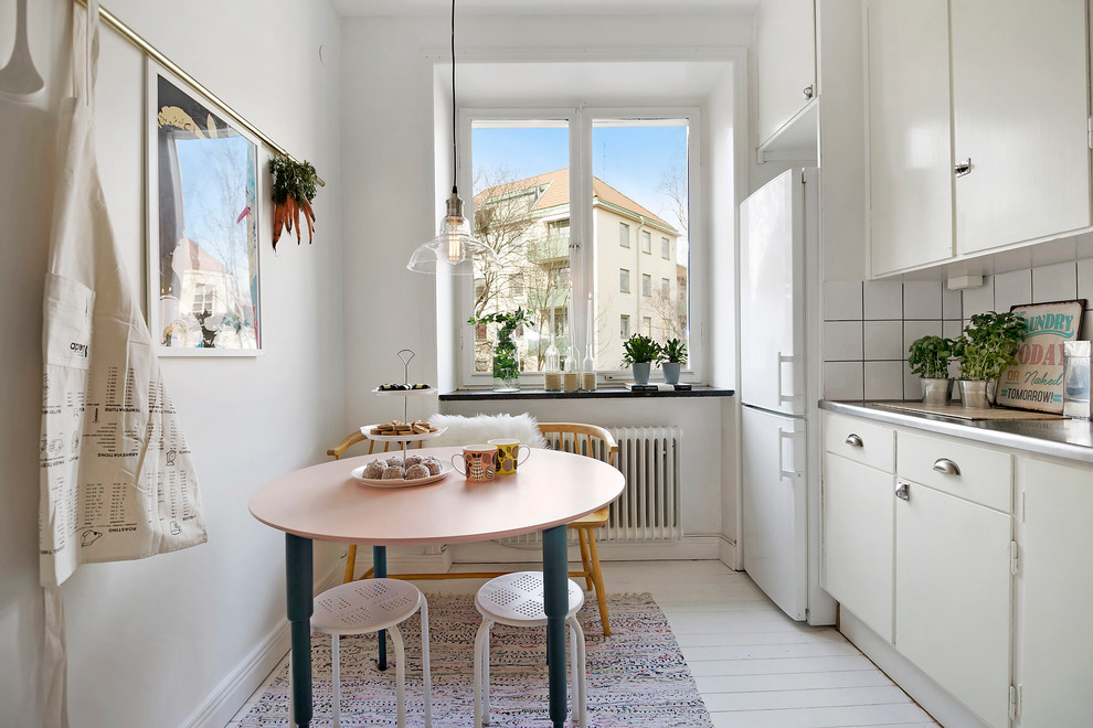 Inspiration for a mid-sized scandinavian single-wall painted wood floor eat-in kitchen remodel in Stockholm with flat-panel cabinets, white cabinets, stainless steel countertops, white backsplash, no island, ceramic backsplash and white appliances