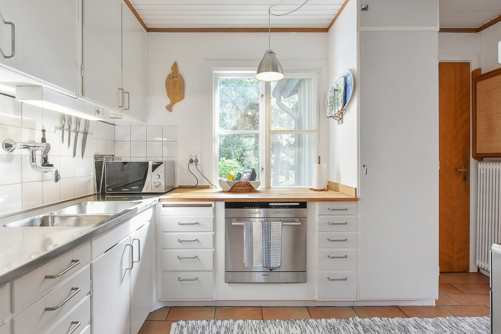 Bild på ett mellanstort skandinaviskt l-kök, med en integrerad diskho, vita skåp, bänkskiva i rostfritt stål, vitt stänkskydd, stänkskydd i keramik och rostfria vitvaror