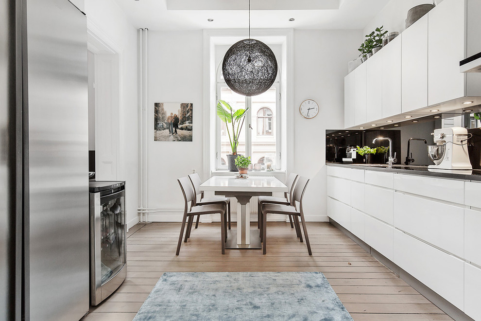 Eat-in kitchen - large scandinavian galley medium tone wood floor eat-in kitchen idea in Stockholm with flat-panel cabinets, white cabinets, black backsplash, stainless steel appliances, no island and granite countertops