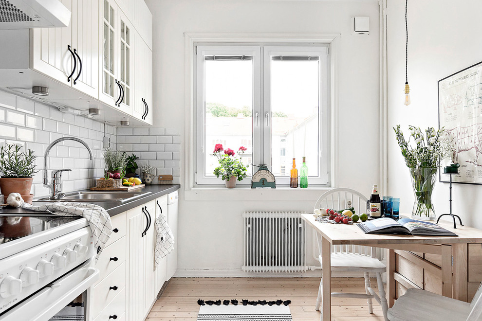 Bild på ett minimalistiskt linjärt kök och matrum, med en enkel diskho, vita skåp, vitt stänkskydd, stänkskydd i tunnelbanekakel, ljust trägolv, släta luckor, vita vitvaror och beiget golv