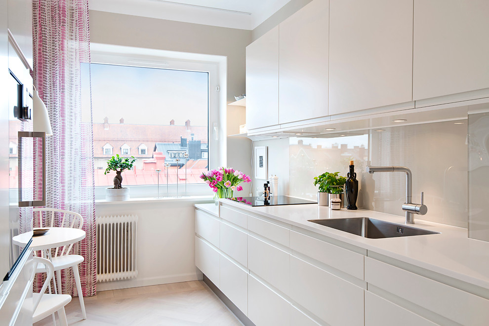 Inredning av ett skandinaviskt mellanstort linjärt kök, med en enkel diskho, släta luckor, vita skåp, laminatbänkskiva, vitt stänkskydd, glaspanel som stänkskydd, rostfria vitvaror och ljust trägolv