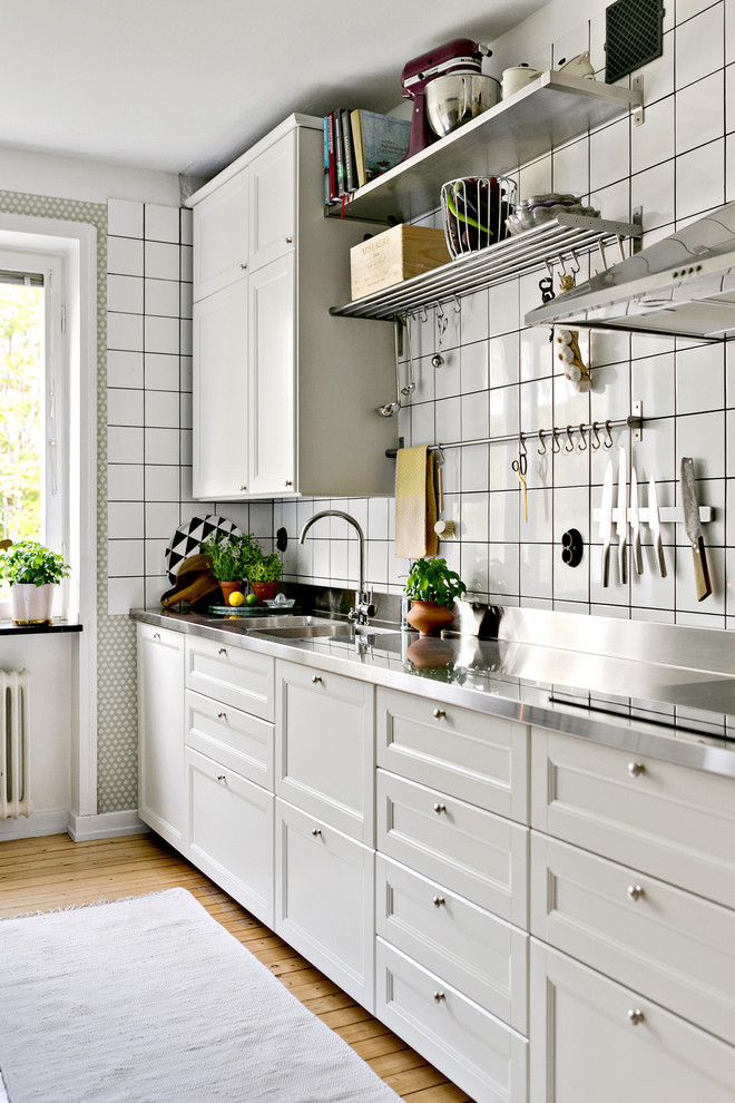 Foto på ett mellanstort vintage linjärt kök med öppen planlösning, med skåp i shakerstil, vita skåp, bänkskiva i rostfritt stål, vitt stänkskydd och stänkskydd i keramik