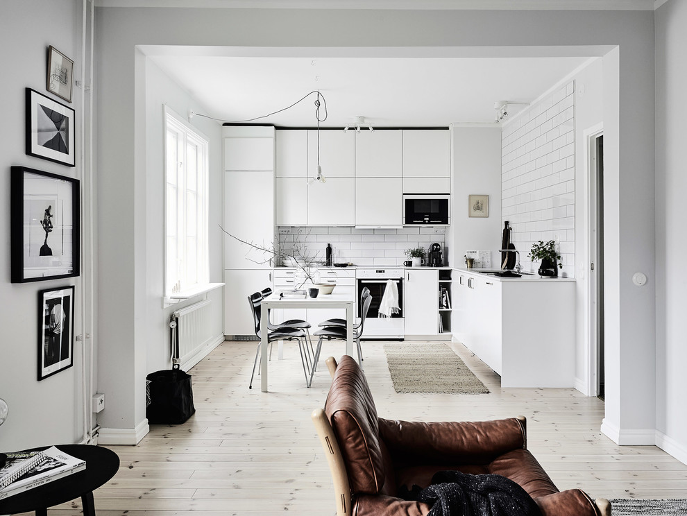 Diseño de cocinas en L nórdica grande sin isla con armarios con paneles lisos, puertas de armario blancas, electrodomésticos blancos y suelo de madera clara