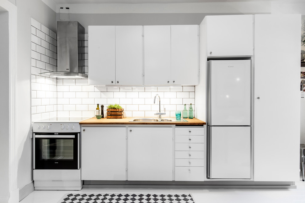 Bild på ett stort minimalistiskt linjärt kök och matrum, med en dubbel diskho, släta luckor, vita skåp, träbänkskiva, vita vitvaror, vitt stänkskydd, stänkskydd i keramik, målat trägolv och vitt golv