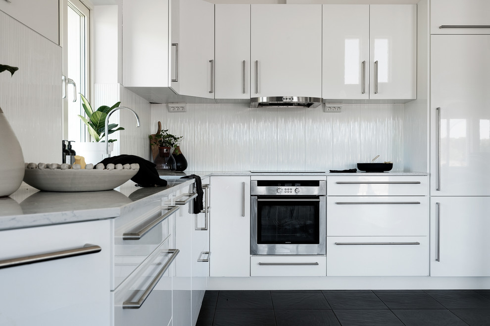 Foto på ett mellanstort nordiskt grå l-kök, med vita skåp, marmorbänkskiva, vitt stänkskydd, svart golv, släta luckor och rostfria vitvaror