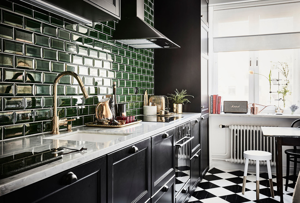 Inredning av ett nordiskt mellanstort linjärt kök och matrum, med en undermonterad diskho, luckor med infälld panel, svarta skåp, grönt stänkskydd, stänkskydd i tunnelbanekakel, svarta vitvaror, marmorbänkskiva, målat trägolv och flerfärgat golv