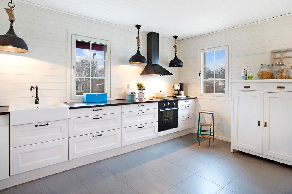 他の地域にあるお手頃価格の広い北欧スタイルのおしゃれなI型キッチン (エプロンフロントシンク、落し込みパネル扉のキャビネット、白いキッチンパネル、黒い調理設備、アイランドなし) の写真
