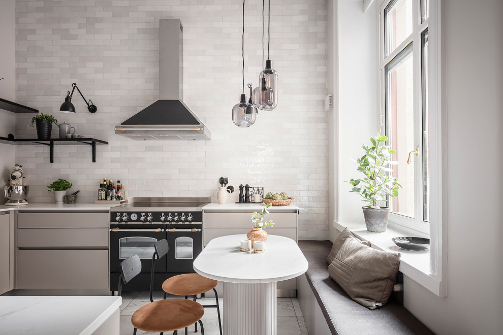 Источник вдохновения для домашнего уюта: угловая кухня в скандинавском стиле с обеденным столом, плоскими фасадами, серыми фасадами, белым фартуком, черной техникой, серым полом и белой столешницей