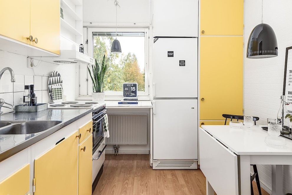 Photo of a medium sized scandi l-shaped kitchen/diner in Other with an integrated sink, flat-panel cabinets, yellow cabinets, stainless steel worktops, white splashback, ceramic splashback, white appliances, no island and medium hardwood flooring.