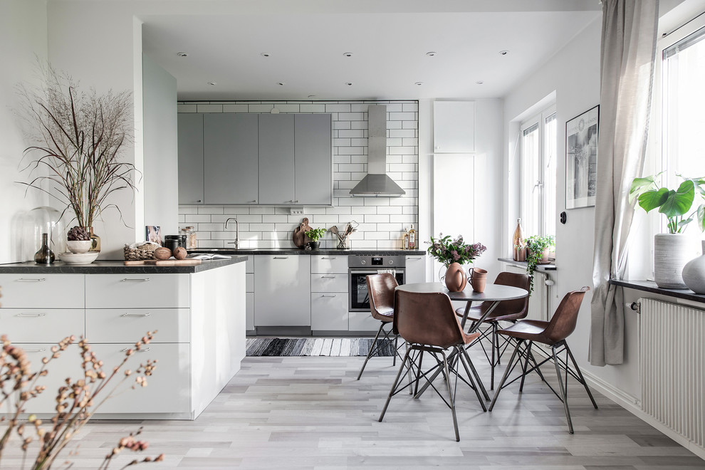 Inredning av ett minimalistiskt mellanstort kök med öppen planlösning, med släta luckor, grå skåp, granitbänkskiva, vitt stänkskydd, stänkskydd i tunnelbanekakel, rostfria vitvaror och grått golv