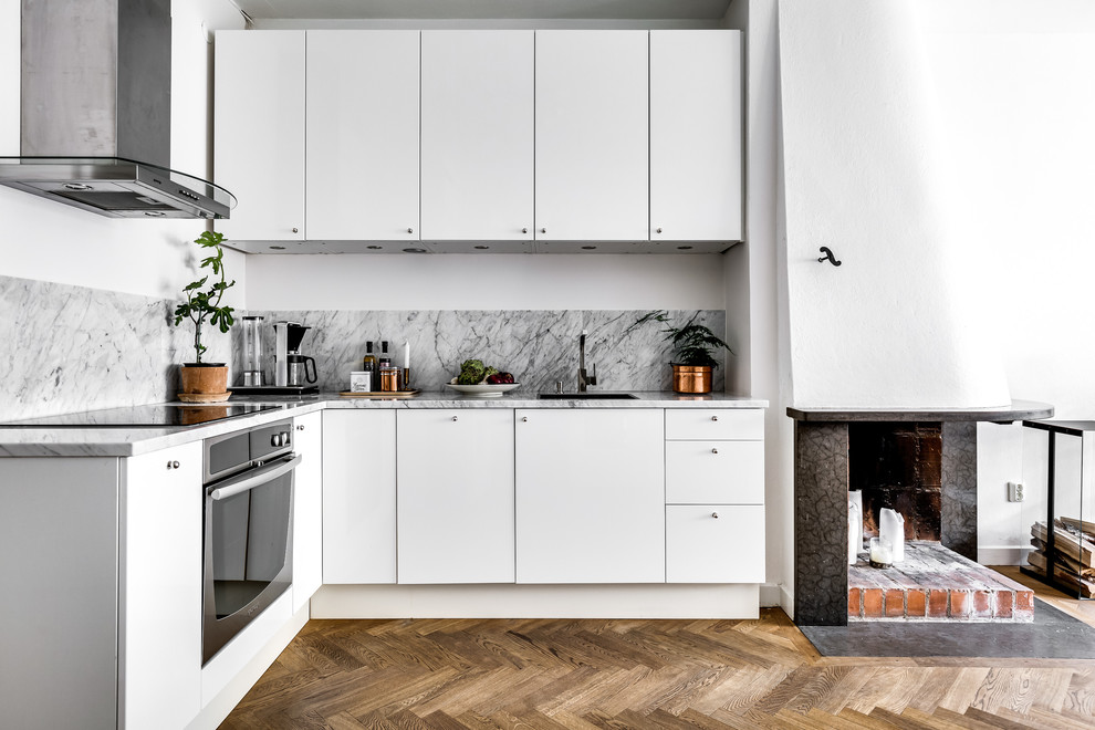 Nordisk inredning av ett litet kök, med släta luckor, vita skåp, marmorbänkskiva och stänkskydd i marmor
