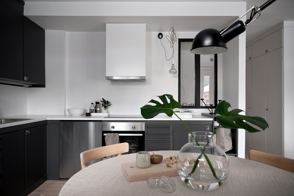 Minimalistisk inredning av ett kök, med en nedsänkt diskho, grå skåp, laminatbänkskiva, vitt stänkskydd, fönster som stänkskydd, rostfria vitvaror, ljust trägolv och vitt golv
