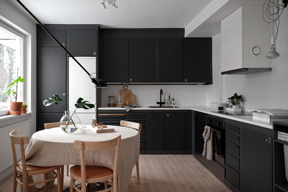 Foto på ett minimalistiskt kök, med en nedsänkt diskho, laminatbänkskiva, vitt stänkskydd, ljust trägolv, släta luckor, svarta skåp, svarta vitvaror och beiget golv