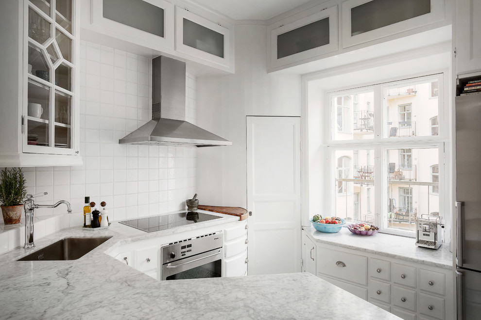 Inredning av ett minimalistiskt avskilt, mellanstort u-kök, med en nedsänkt diskho, luckor med upphöjd panel, vita skåp, marmorbänkskiva, vitt stänkskydd, stänkskydd i porslinskakel och rostfria vitvaror