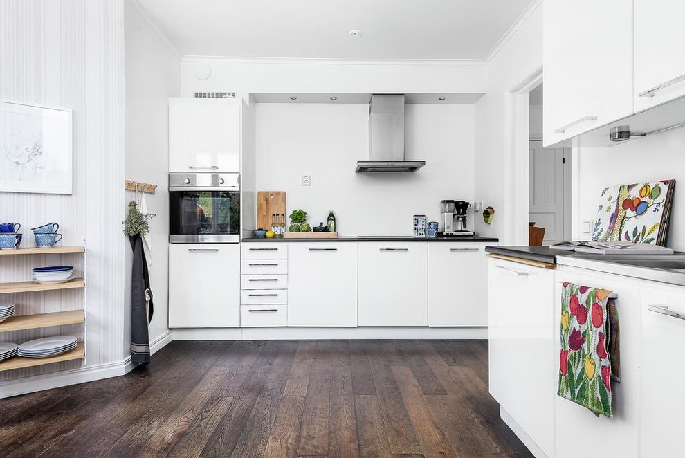 This is an example of a scandi l-shaped kitchen in Stockholm with flat-panel cabinets, white cabinets, stainless steel appliances, dark hardwood flooring and no island.