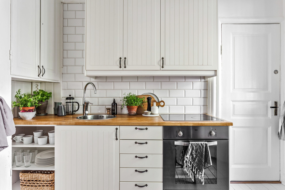 Photo of a scandi single-wall kitchen in Gothenburg with white cabinets, wood worktops, white splashback, stainless steel appliances, beige worktops, a built-in sink, metro tiled splashback, no island and flat-panel cabinets.