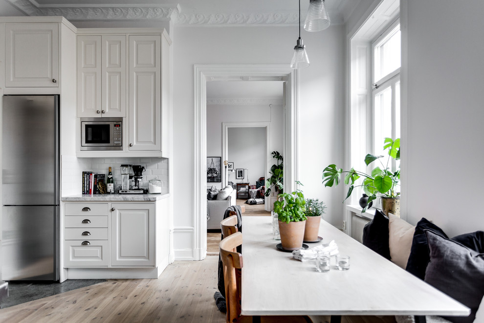 Medium sized farmhouse open plan kitchen in Stockholm with light hardwood flooring.