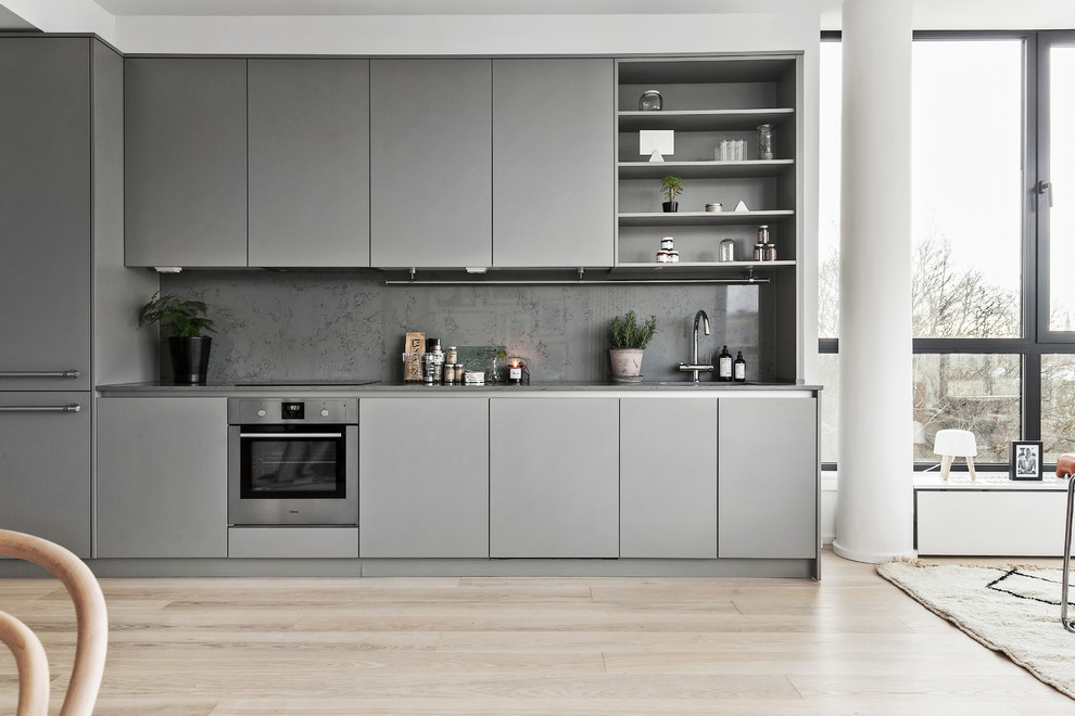 Bild på ett mellanstort minimalistiskt linjärt kök med öppen planlösning, med släta luckor, grå skåp, grått stänkskydd, rostfria vitvaror, ljust trägolv och marmorbänkskiva