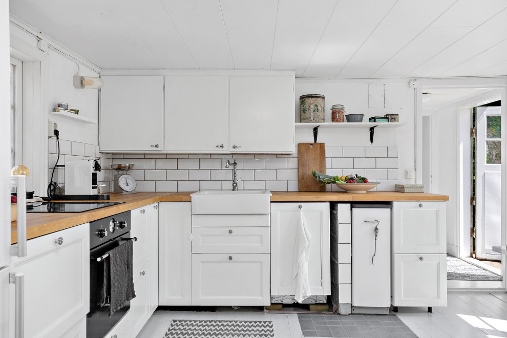 Idéer för ett mellanstort minimalistiskt beige l-kök, med en rustik diskho, luckor med infälld panel, vita skåp, träbänkskiva, vitt stänkskydd, stänkskydd i tunnelbanekakel, svarta vitvaror och grått golv