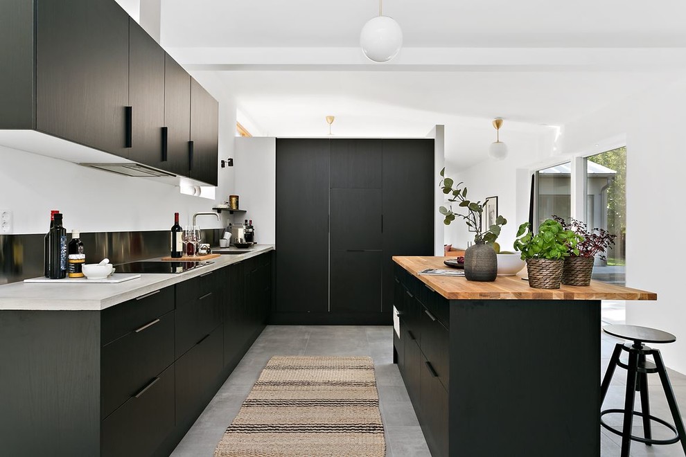 Foto de cocinas en L nórdica con armarios con paneles lisos, puertas de armario negras, encimera de madera, electrodomésticos con paneles, una isla y suelo gris