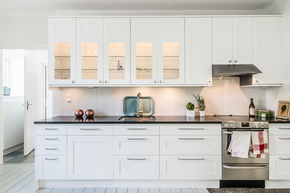 Inspiration för stora minimalistiska linjära kök, med en undermonterad diskho, skåp i shakerstil, vita skåp, vitt stänkskydd, rostfria vitvaror och målat trägolv