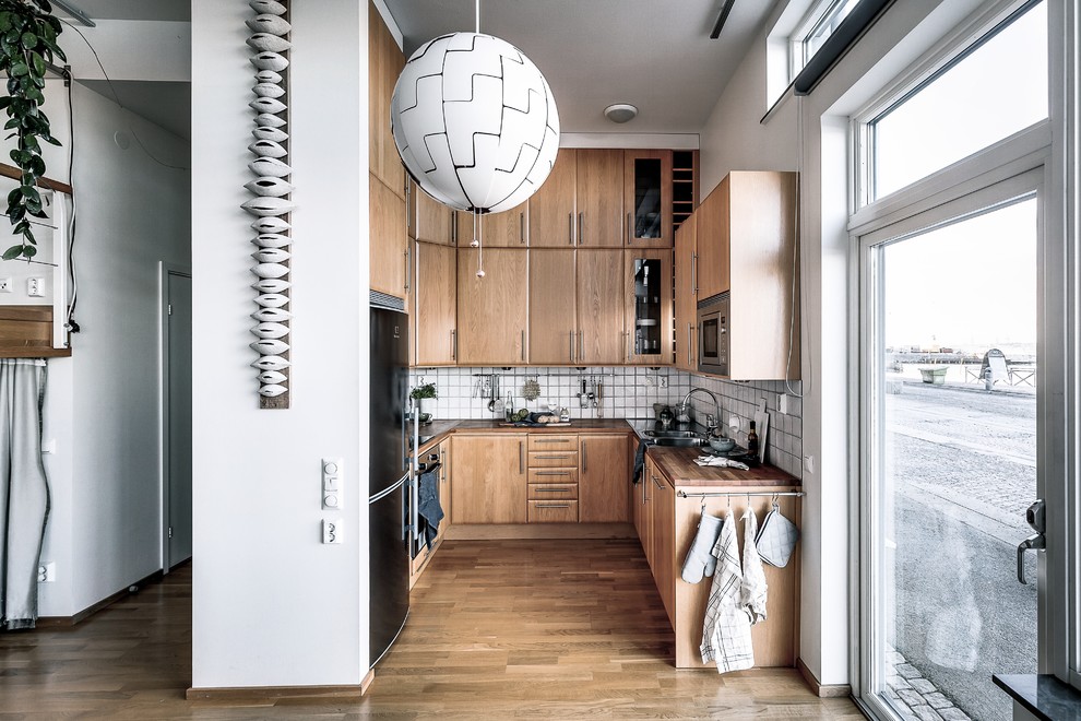 Photo of a scandi u-shaped kitchen in Stockholm with a built-in sink, flat-panel cabinets, medium wood cabinets, wood worktops, white splashback, stainless steel appliances, medium hardwood flooring, no island, brown floors and brown worktops.