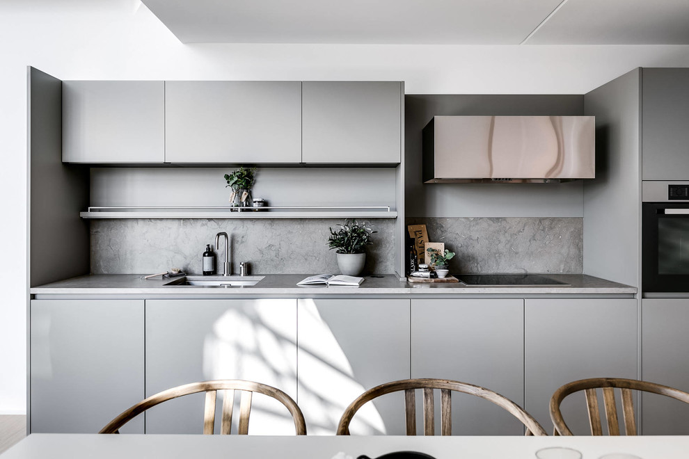 Idéer för att renovera ett skandinaviskt grå linjärt grått kök och matrum, med en undermonterad diskho, släta luckor, grå skåp, grått stänkskydd och svarta vitvaror