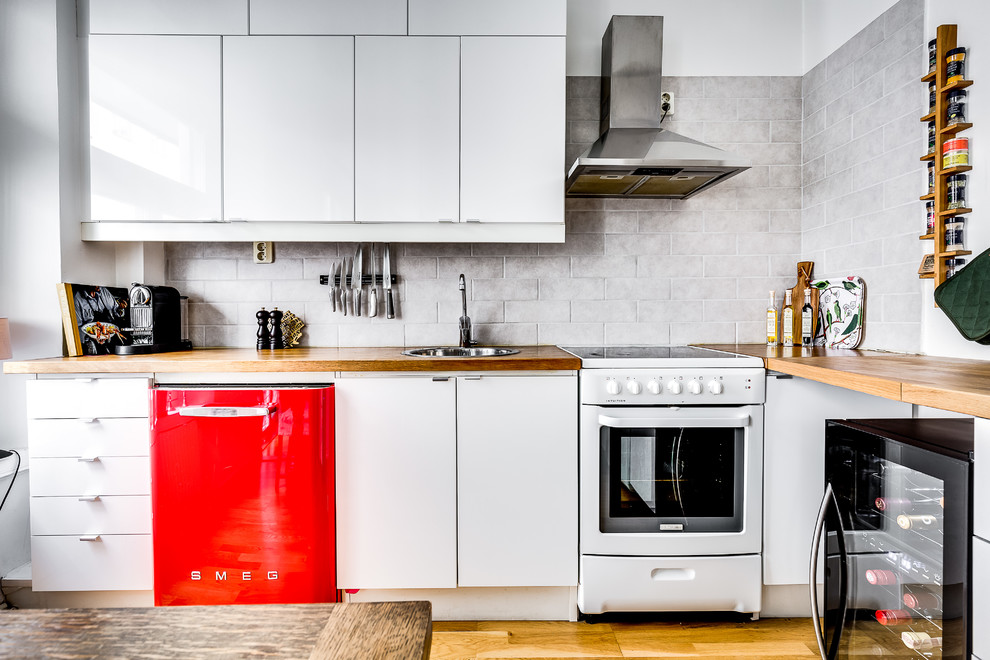 Exemple d'une cuisine scandinave en L avec un placard à porte plane, des portes de placard blanches, une crédence grise, une crédence en carrelage métro, un électroménager de couleur, un sol en bois brun et un sol marron.